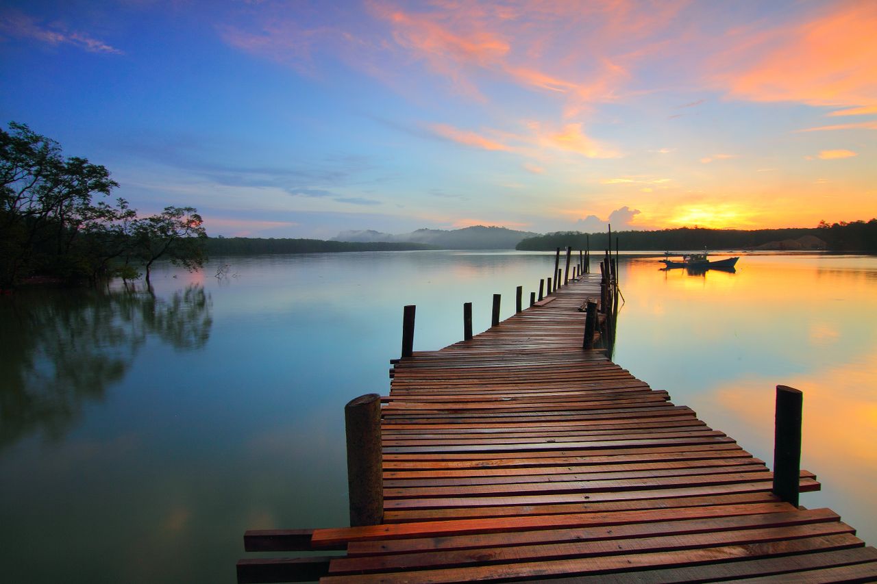 A lone fishing boat on calm water beneath a glowing orange and pink sunset